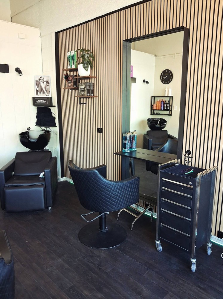 Styling station inside the salon, with oak slat walls, a black quilted chair and a large mirror